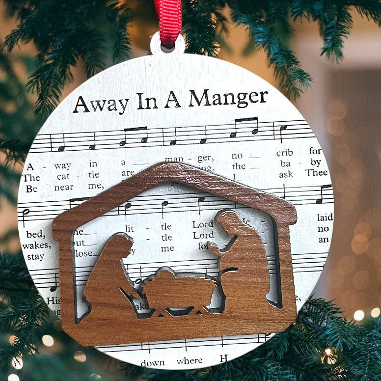 Decorative Christmas ornament with nativity scene and 'Away in a Manger' lyrics on a tree.